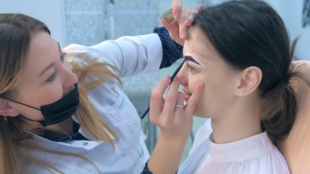 Cosmetologist está colorindo sobrancelhas da mulher com tinta marrom na clínica de beleza . — Vídeo de Stock