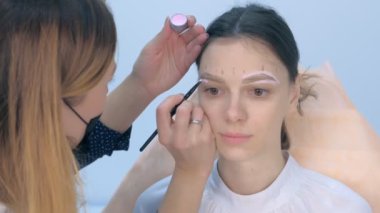 Cosmetologist painting brush shape of eyebrows woman before tint procedure.