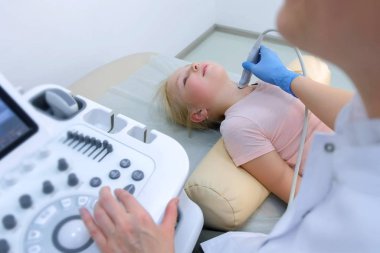 Hasta çocuk tiroid bezini ultrason tarayıcı kullanarak muayene eden doktor..