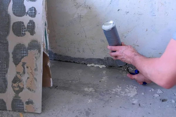 Arbeiter füllt Riss zwischen Wand und Zementboden mit Schaumstoff im Raum. — Stockfoto