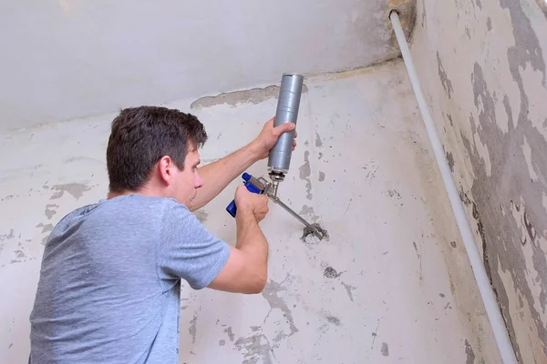 Mann stopft Loch in Wand aus Betonplatte und montiert Schaum für Reparaturen zu Hause. — Stockfoto