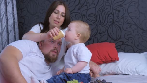 家族のお母さん、お父さんと赤ちゃんの女の子は家で一緒にブドウとアイスクリームを食べています. — ストック動画