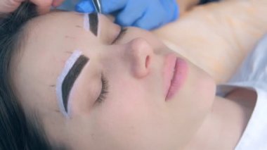 Beautician plucking eyebrows with tweezers to woman face in beauty salon.