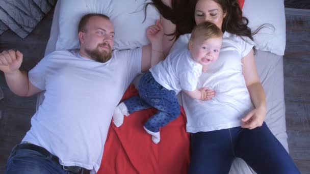 Retrato familiar de mamá, papá y bebé acostados en la cama en casa, vista superior . — Vídeos de Stock