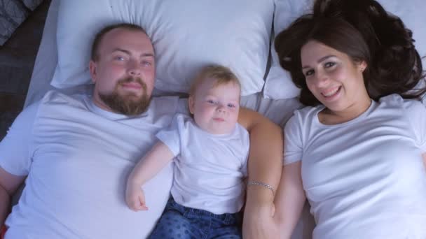 Rodzinny portret mamy, taty i dziecka leżących w łóżku w domu całujących się dzieci. — Wideo stockowe