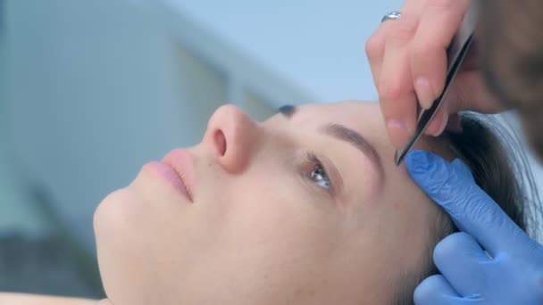 Kosmetička škubání obočí s pinzetou na ženu v salonu krásy, detailní záběr. — Stock video