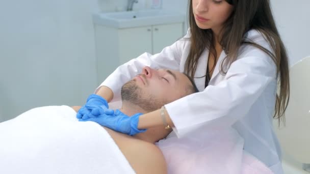 Kosmetolog w rękawiczkach nakłada krem na skórę człowieka do masażu szyi. — Wideo stockowe