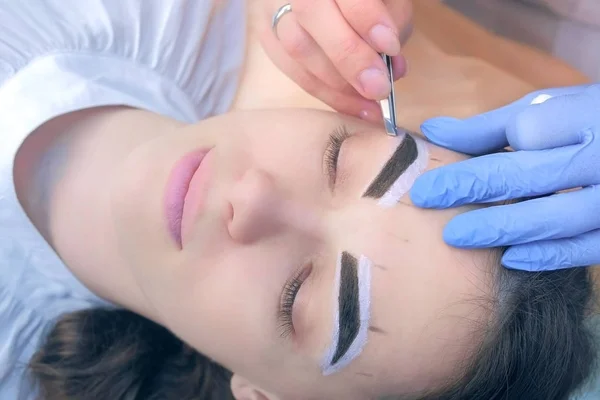 Esteticista arrancando sobrancelhas com pinças para rosto de mulher no salão de beleza . — Fotografia de Stock