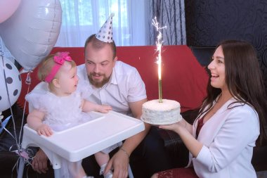Mom gives daughter a cake with candle on birthday party of one year baby girl.
