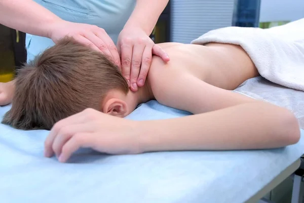 Médico massagista fazendo massagem ao menino adolescente nos ombros e pescoço na clínica . — Fotografia de Stock
