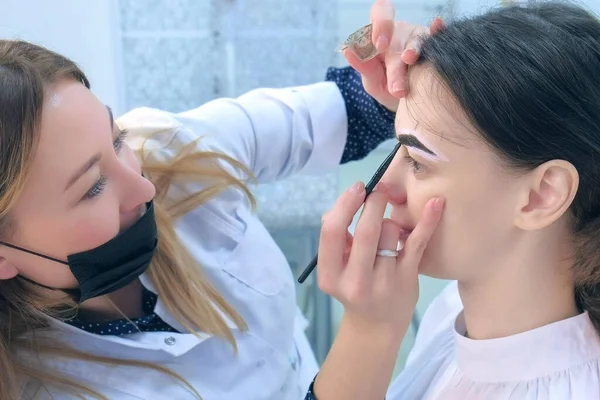 Cosmetólogo está teñiendo las cejas de mujer con pintura marrón en clínica de belleza . — Foto de Stock