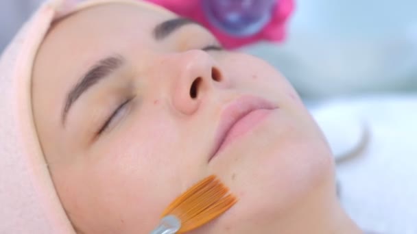 Cosmetologo applicare lozione peeling sul viso delle donne utilizzando pennello in clinica. — Video Stock