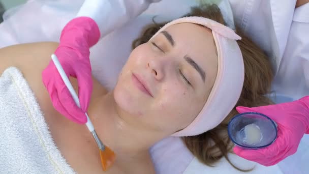 Cosmetoloog arts aanbrengen masker op vrouwen gezicht met behulp van borstel in schoonheidskliniek. — Stockvideo