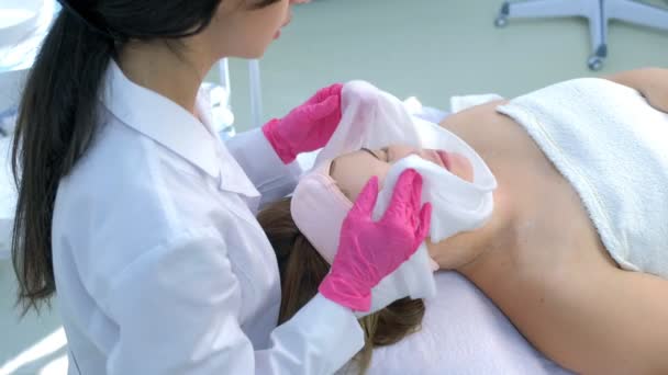 Cosmetoloog veegt hydraterende masker van vrouwen gezicht met behulp van warme handdoek. — Stockvideo