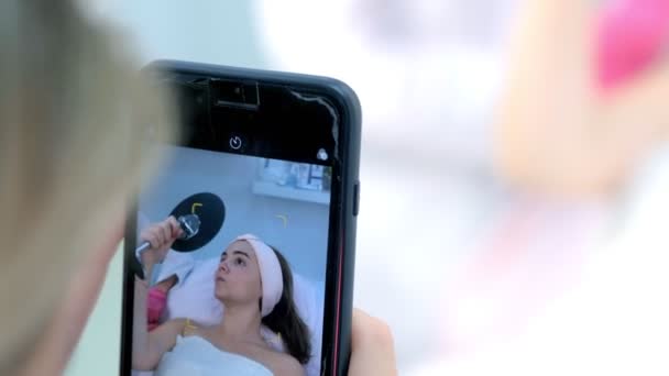 Fazendo uma foto de mulher jovem no procedimento de cosmetologia no smartphone . — Vídeo de Stock