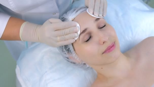 Cosmetologue essuie les femmes visage avec des tampons de coton dans la clinique de beauté, gros plan. — Video