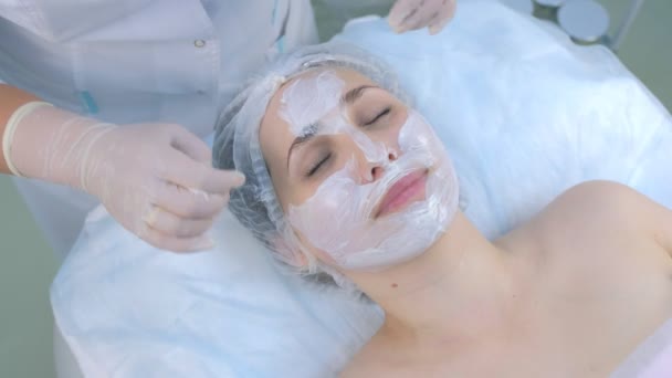 Beautician is applying facial moisturizing mask on woman face in beauty clinic. — Stock Video