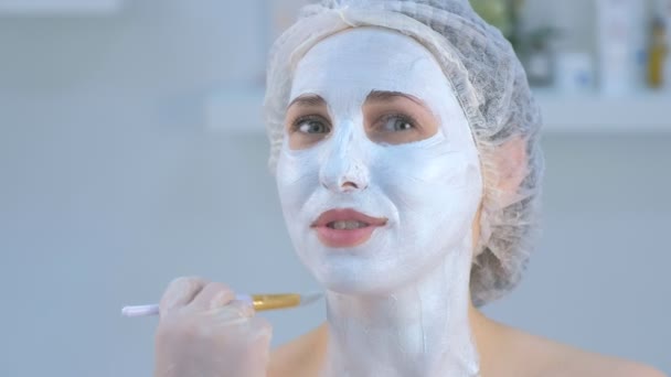 Cosmetologist está aplicando máscara hidratante facial no rosto da mulher usando escova . — Vídeo de Stock