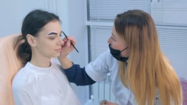 Cosmetologist is tinting woman eyebrows with brown paint in beauty clinic.