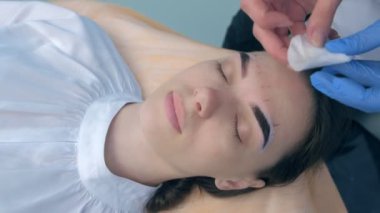 Kozmetik uzmanı, güzellik kliniğinde kadın kaşlarından kahverengi kına temizliyor..