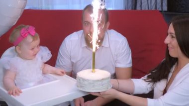 Mom gives daughter a cake with candle on birthday party of one year baby girl.