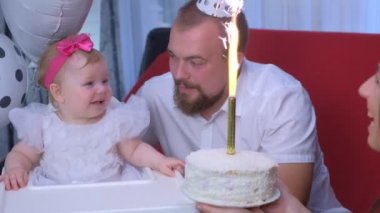 Mom gives daughter a cake with candle on birthday party of one year baby girl.