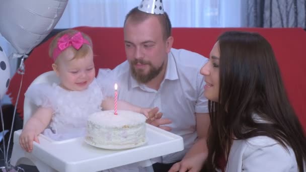 Familie portret mam, vader blazen kaars op taart op baby meisjes eerste verjaardag. — Stockvideo