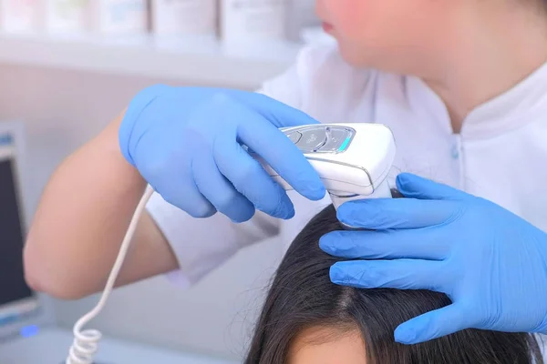 Orvos trichologist vizsgálja női betegek szőrszálak segítségével dermatoscope klinikán. — Stock Fotó