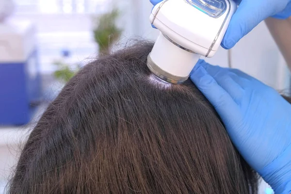 Dokter tricholoog onderzoekt vrouwelijke patiënten haren met behulp van dermatoscoop in de kliniek. — Stockfoto