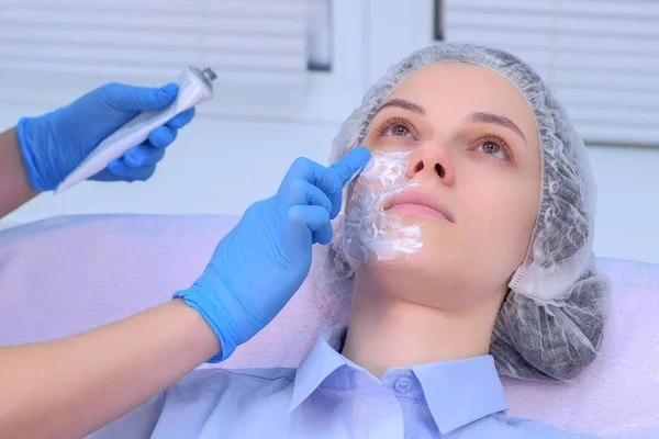 Cosmetoloog is het aanbrengen van crème met verdoving op patiënten gezicht, close-up zicht. — Stockfoto