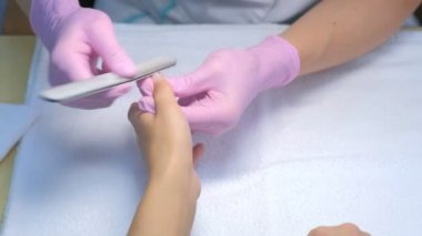 Eldivenlerde manikürcü ustası müşterilerin tırnaklarını cilalıyor dosya kullanıyor, elleri yakın çekim yapıyor..