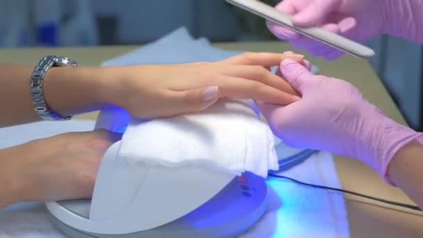 Manicure polijsten klanten nagels met behulp van bestand, andere hand drogen in Uv lamp. — Stockvideo