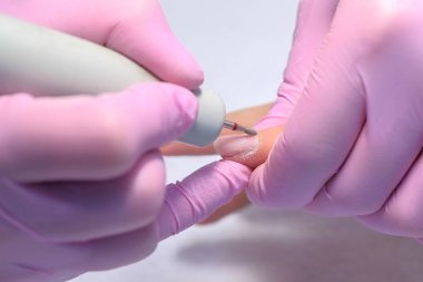 Manikür ustası elektrikli çivi matkabı kullanarak müşteri için manikür yapıyor.