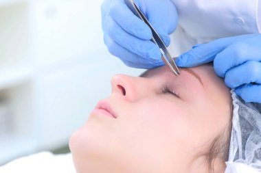 Kozmetik uzmanı, kadın için cımbızla kaş kılları yoluyor..