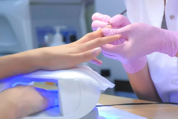 Manicure mestre clientes pintura unhas gel goma laca, outra mão em lâmpada UV. — Fotografia de Stock
