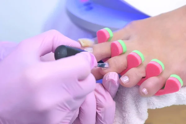 Maestro pedicurista está cubriendo pintar clientes dedos de los pies uñas shellac, primer plano. —  Fotos de Stock