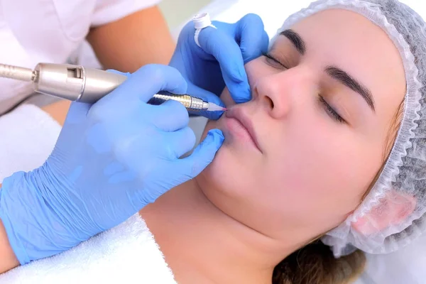 Cosmetoloog is het aanbrengen van permanente make-up op de lippen met behulp van tattoo machine. — Stockfoto