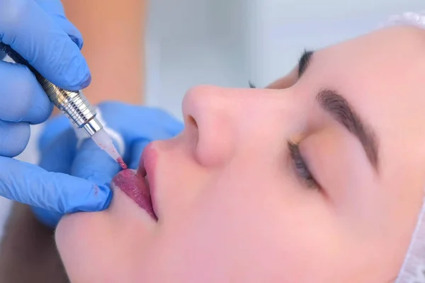 Cosmetoloog het maken van lippen microblading procedure voor meisje met behulp van tattoo machine. — Stockfoto