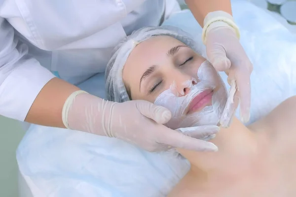 Cosmetologist aplicando máscara hidratante facial no rosto da mulher na clínica de beleza . — Fotografia de Stock