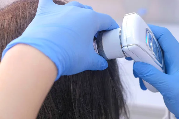 Dokter tricholoog onderzoekt vrouwelijke patiënten haren met behulp van trichoscoop in de kliniek. — Stockfoto