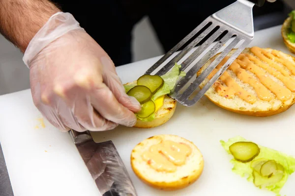 Der Koch bereitet die Hamburger in der Küche zu. Brötchen, Gemüse, Püree — Stockfoto