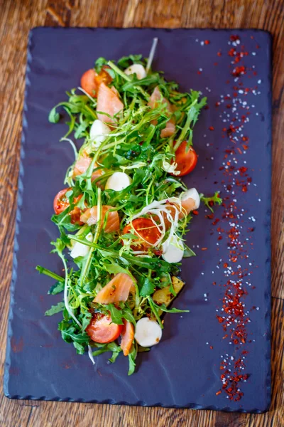 Салат с соленым лососем с рукколой и моцареллой на черном — стоковое фото