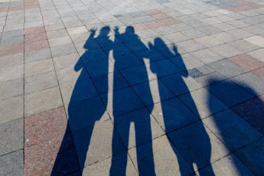 Üç kişi bir kaldırım döşeme üzerinde gölgeler.