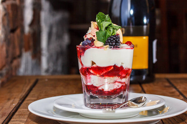 A dessert of fresh yoghurt, jam and fresh berries in a glass.