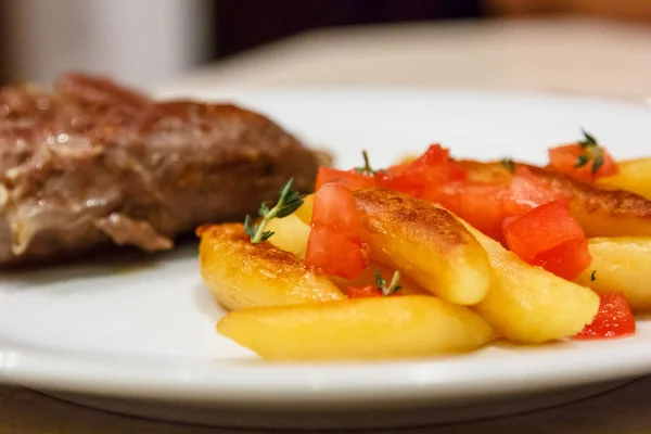 Fried potatoes with tomatoes, a sprig of thyme and roasted meats — Stock Photo, Image