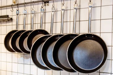 Beyaz karo duvara karşı bir raf siyah tava vardır.