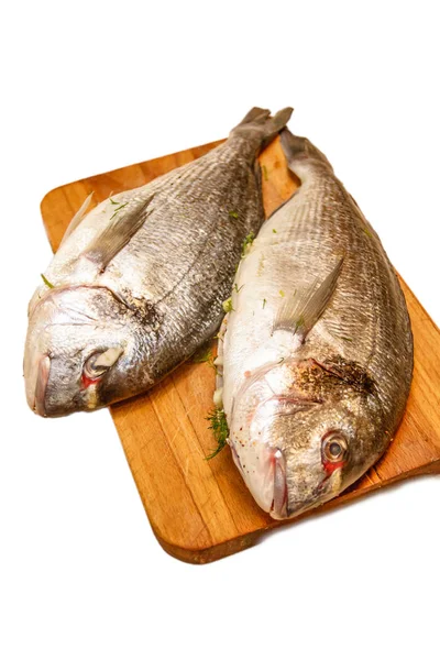 Zwei Fischdorados liegen auf einem Holzbrett auf weißem Hintergrund. — Stockfoto