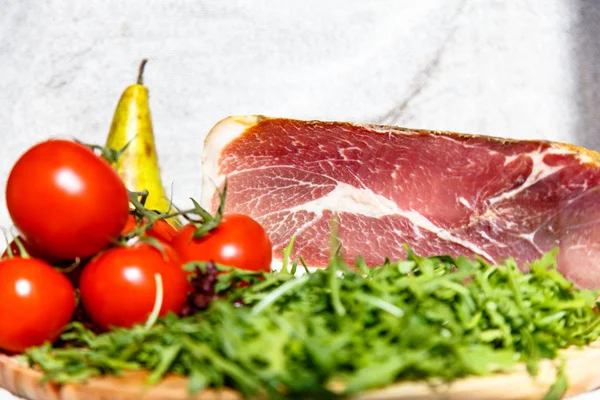 Il prosciutto italiano è sul bancone con rucola e pomodori . — Foto Stock