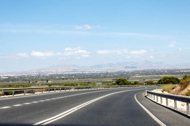 Road, alanlar ve dağlar arka planda.