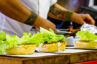 Şef sığır eti, salata ve sebzeli bir burger hazırlar..
